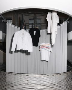 Black and white male and female clothes hanging on display in a white room.