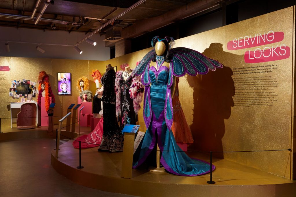 An extravagant blue and purple gown complete with wings, on display alongside hues of orange, blue and black gowns on display.