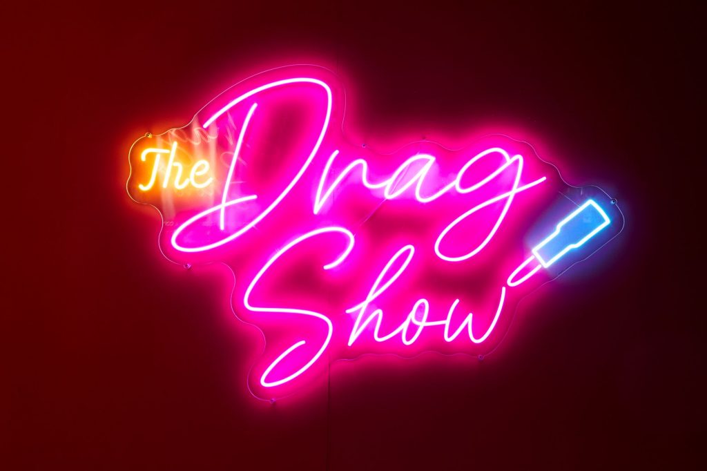 A pink neon light up sign with yellow and a blue lipstick with the words, 'The Drag Show'.