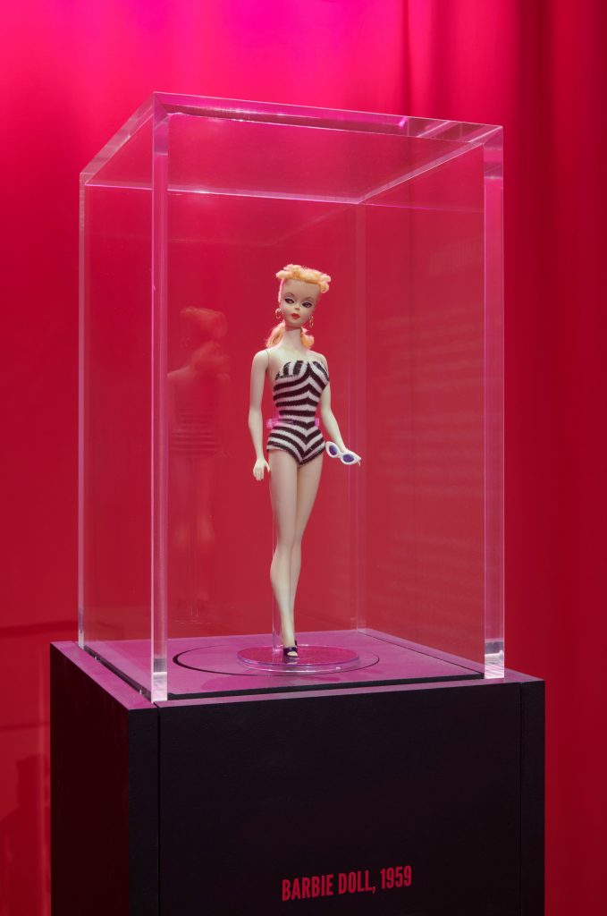 A doll wearing a striped black a white bathing suit.