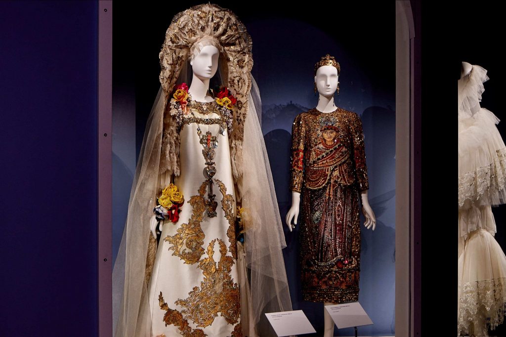 Two female mannequins on display. Left: White dress complete with veil, gold headdress and gold embellishments on the dress. Right: Brown dress with embellishments and quarter length sleeves.