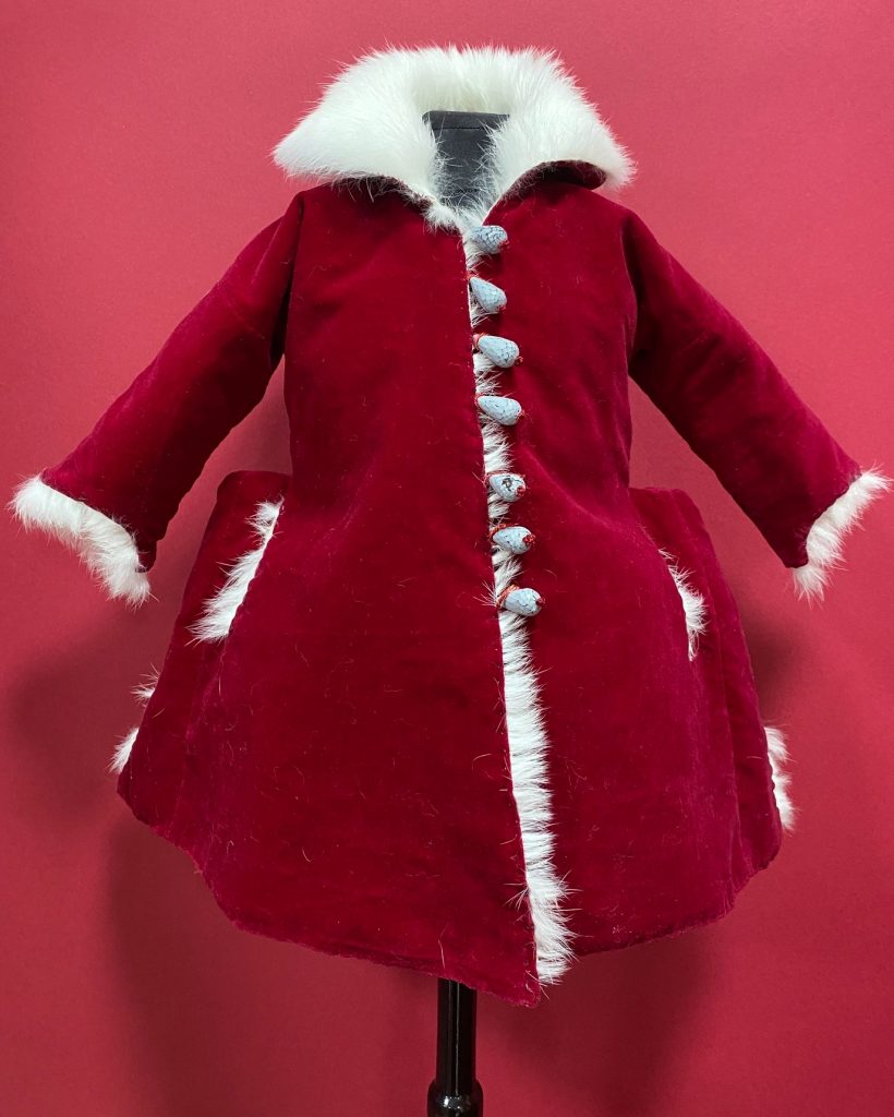 A child's red coat with white fluffy buttons, white cuffs and half hood.