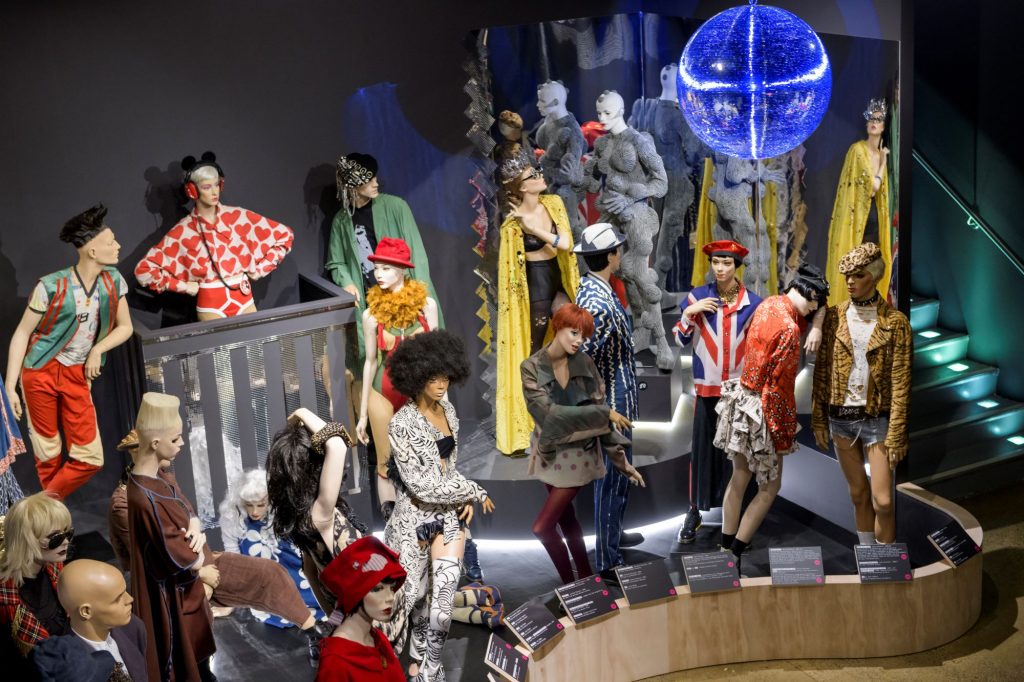 A group of male and female mannequins wearing club inspired outfits, in bright hues of blue, red, yellow, green, orange and silver.