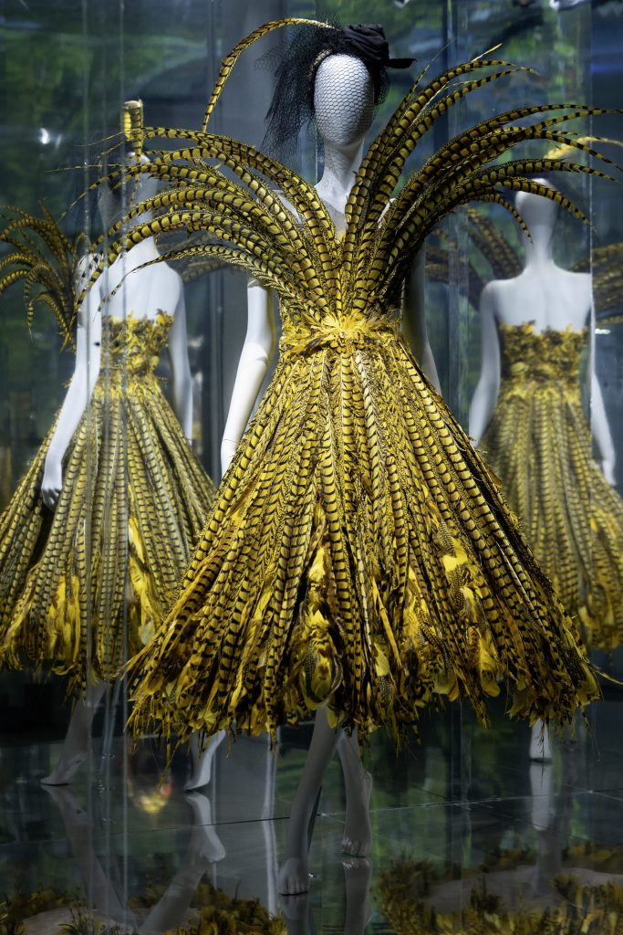 mannequin with dress made of yellow and black feathers with image reflected behind