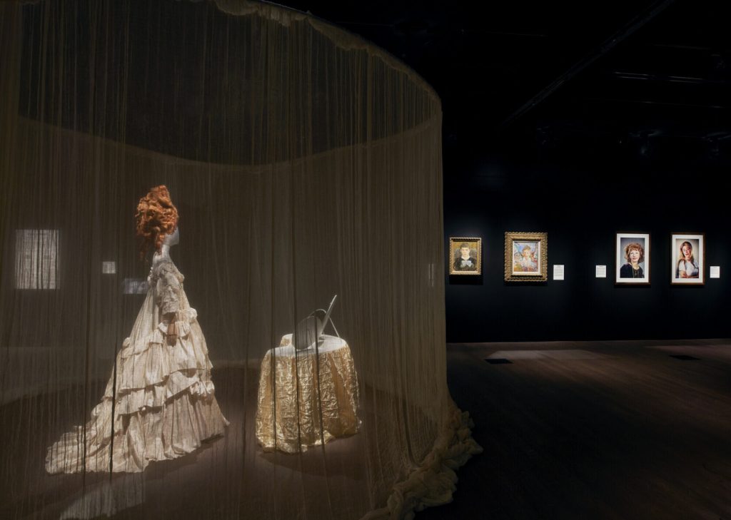 A mannequin wearing a tall ginger wig and wearing a long white ruffled gown.