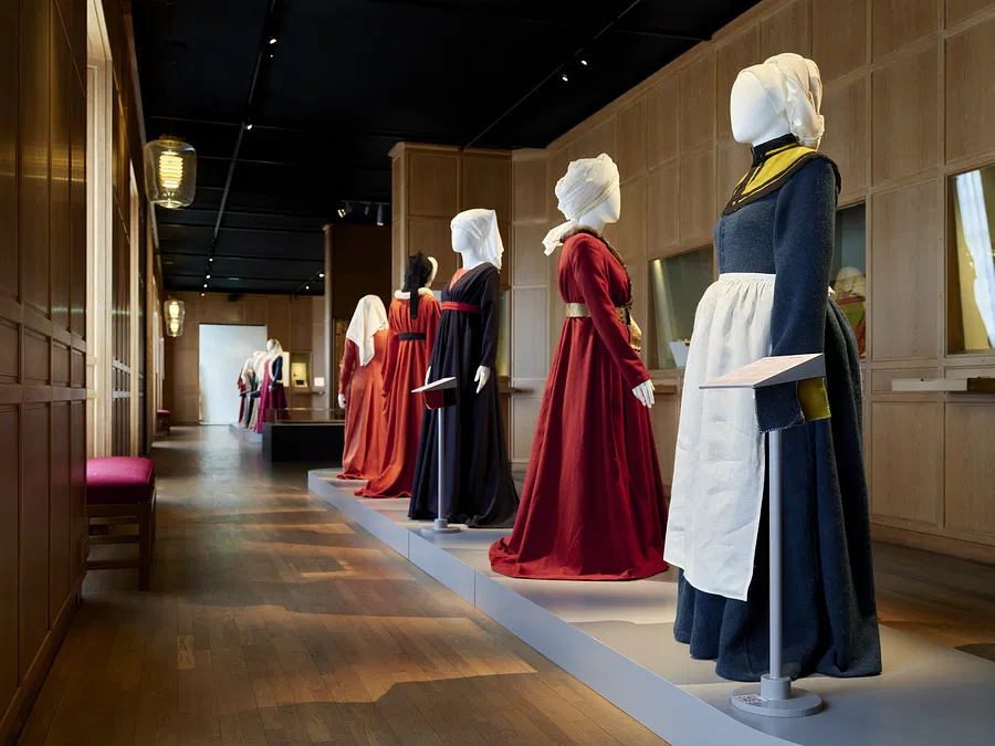 mannequins in gallery from side view in mediaeval dresses with aprons and headwear