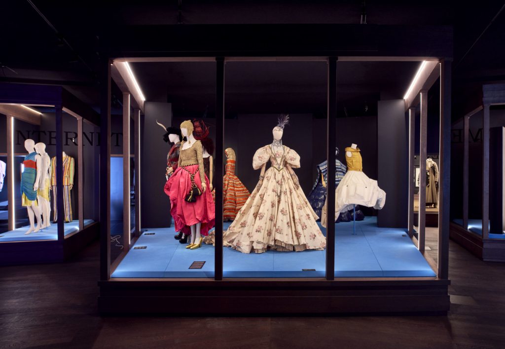 A group of historical female costumes in hues of white, pink, yellow and black.