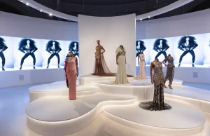 Seven female mannequins wearing different styles of evening gowns all full length. Colours of gowns are in hues of pink, red, silver, gold and white.