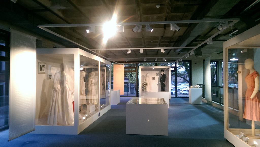 Exhibition display featuring men and women mannquins dressed in various bridal gowns and suits. Colours include white, ivory, cream, and black.