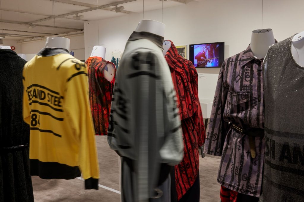 Eight garments on mannequins on display in hues of yellow, red, black and grey.