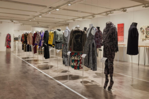 Two rows of mannequins all wearing a mixture of male and female clothing in hues of black, red, yellow, and brown.