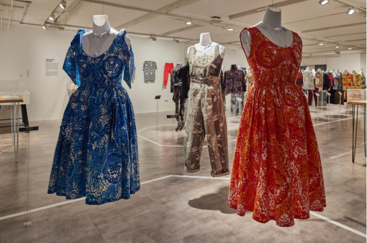 Three female mannequins on display. (Left) scoop neckline blue summer dress, (Right) right summer dress with scooped neckline. (Centre back) Two piece crop top and trousers in black and gold.