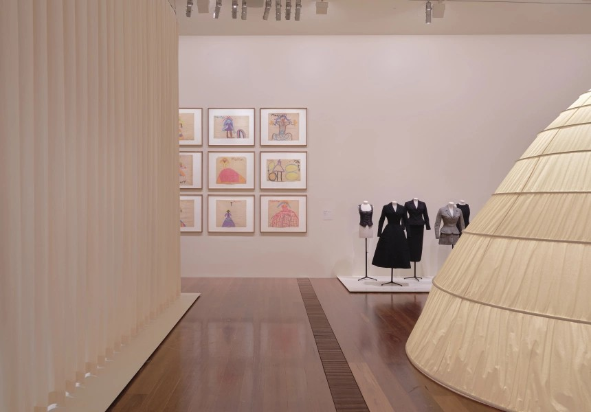 mannequins in gallery with paintings in background and curved arch shaped installation in foreground