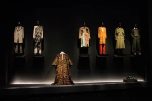A collection of menswear in hues of gold, black, orange and yellow. Outfits are displayed on a black stage.