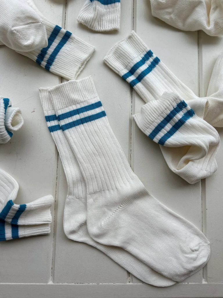 A collection of white socks with blue stripes. Some of the socks are paired, crumpled up and laid out flat.