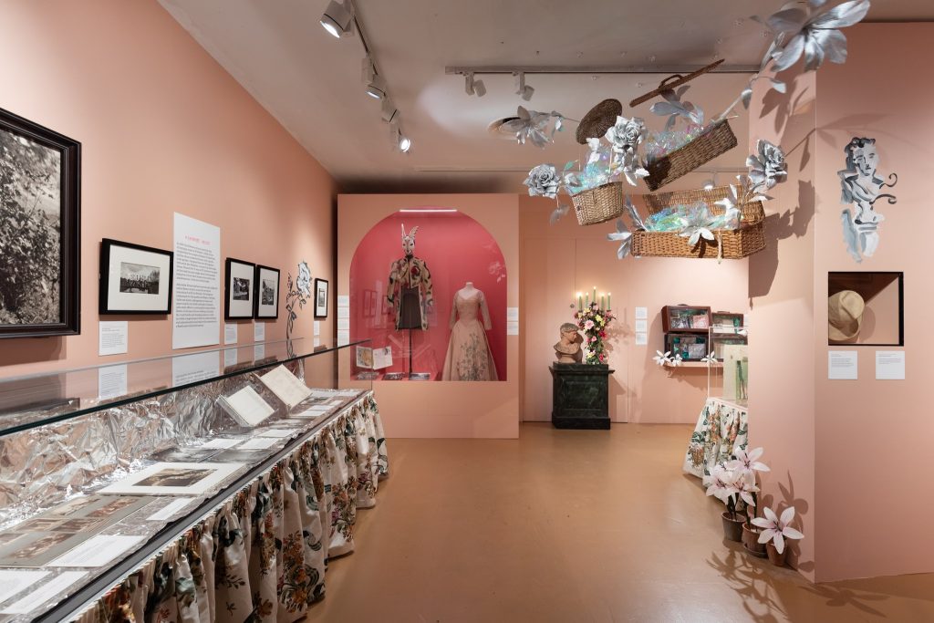 A room with documents on display .Two outfits in hues of pink, florals and embroidery.