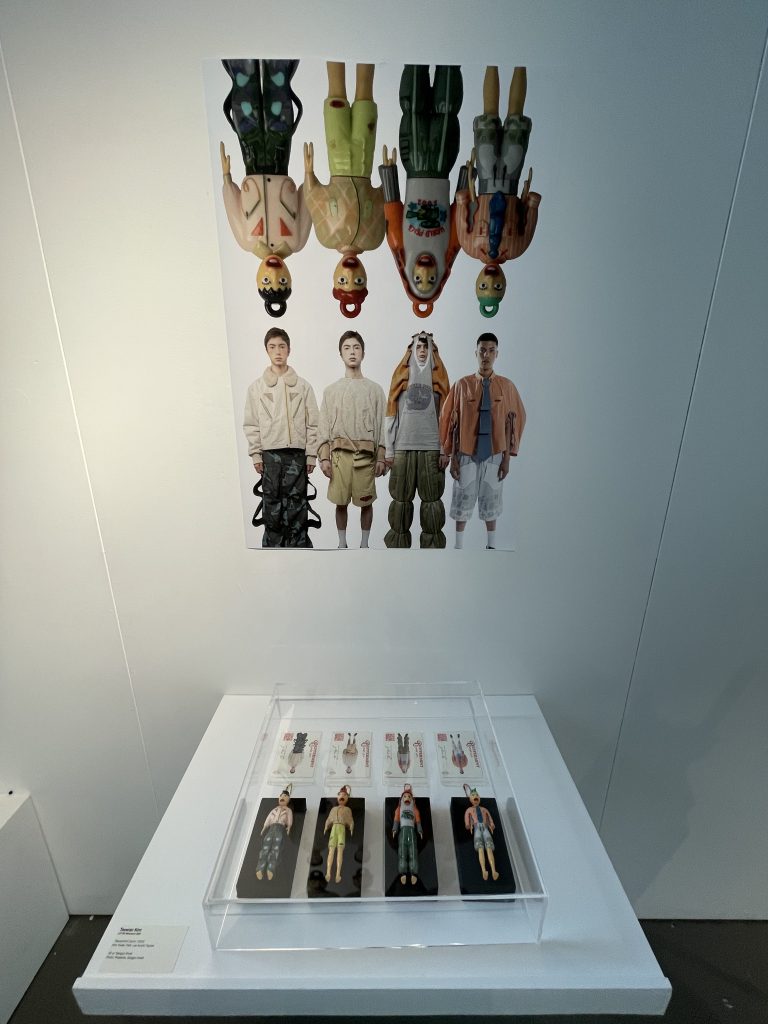 photo of 8 male figures in rows of 4 with top row upside down, and 4 male dolls in vitrine