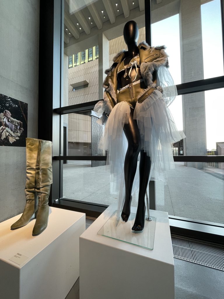 mannequin on display with tutu beside a pair of boots on plinth
