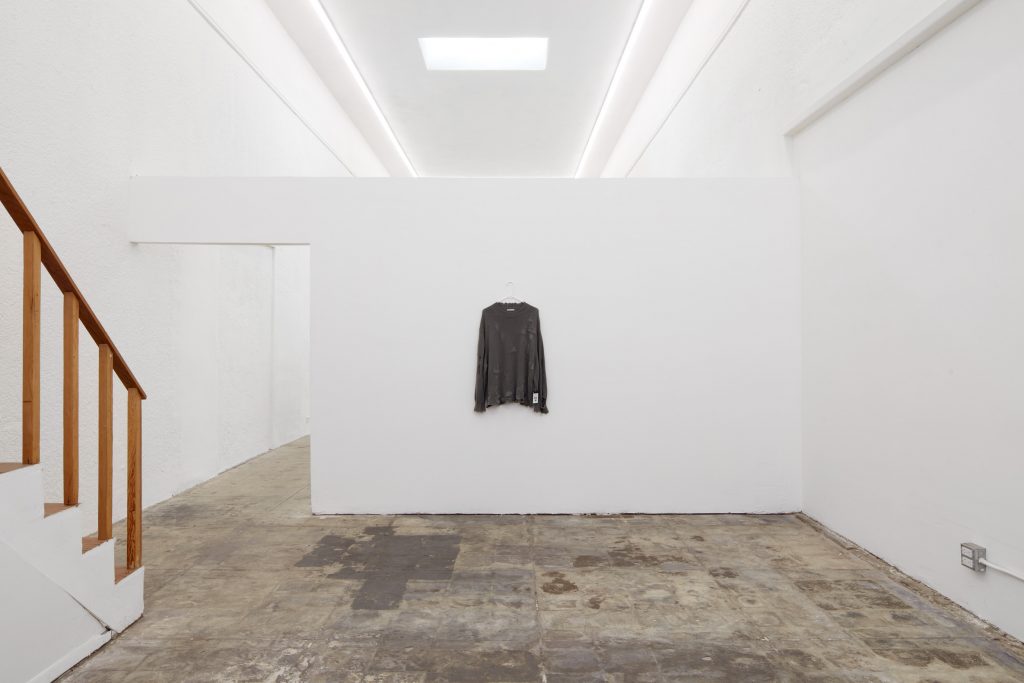 A white installation room displaying a brown sweatshirt on the wall.