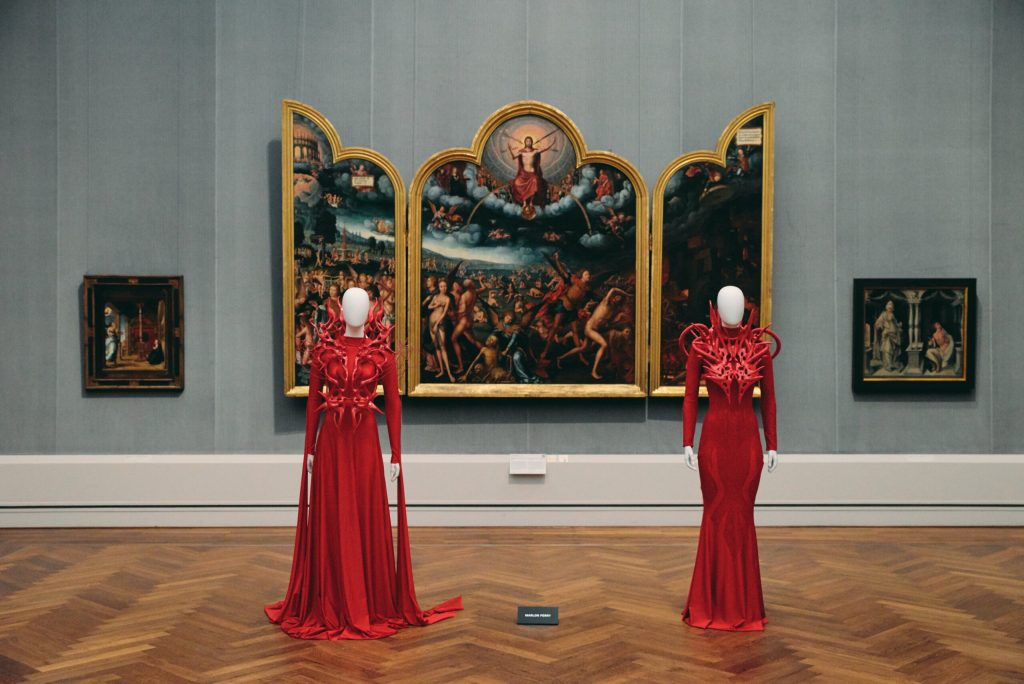 Two mannequins wearing long deep red and long sleeves dresses.