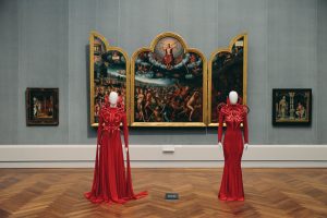 Two mannequins wearing long deep red and long sleeves dresses.