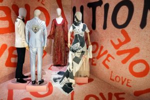 Four mannequins wearing dresses and suits in hues of blue, red, green and black.