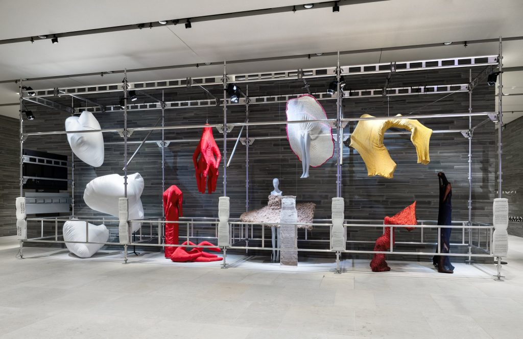 An installation of garment like shapes in hues of red, white, yellow and blue.