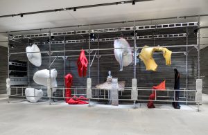 An installation of garment like shapes in hues of red, white, yellow and blue.