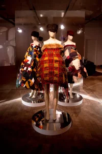 Three mannequins wearing short sleeve-less dresses in hues of brown, orange, green and black.