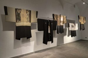Five kimonos on display in hues of gold, black and white.