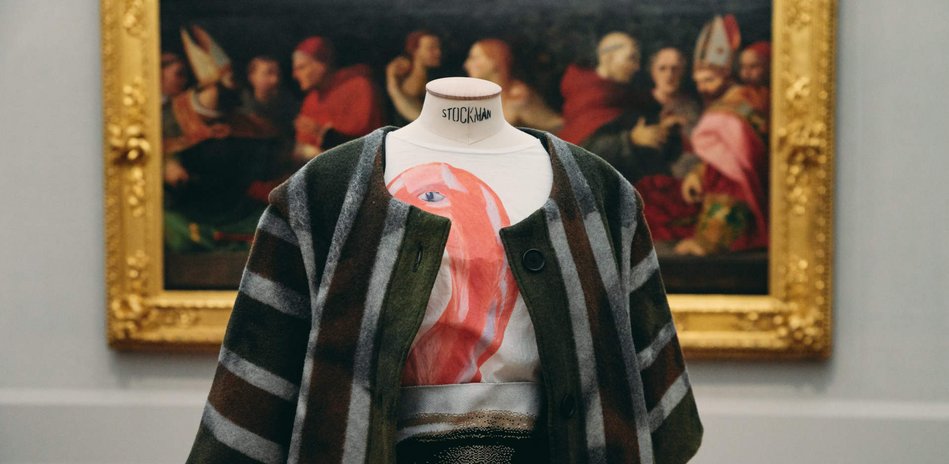 A mannequin wearing a black grey striped cardigan and a white with red motif T-shirt.