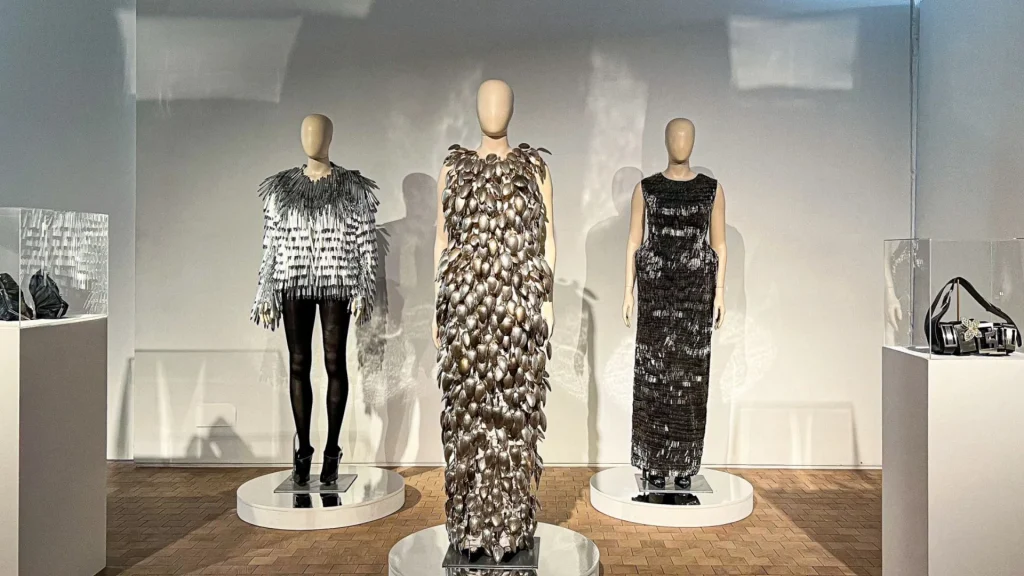 Three mannequins dressed in silver, black and grey full length dresses and trousers.